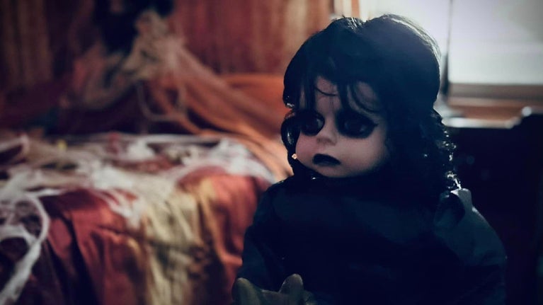 A large creepy looking doll on a rocking horse inside a dimly lit room